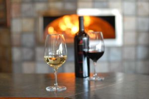 Glass of white wine and red wine, bottle of wine in front of wood fired oven