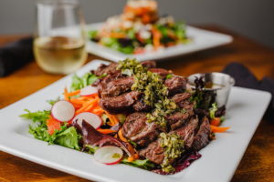 steak salad and second salad on table with wine glass